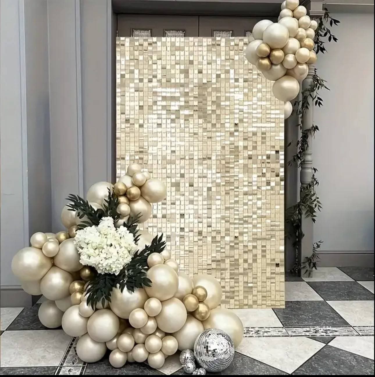 Gold shimmer-wall panels with ivory and champagne balloon clusters at the base, white hydrangea and disco balls at the foot, set in an entrance with a black-and-white chequered marble floor